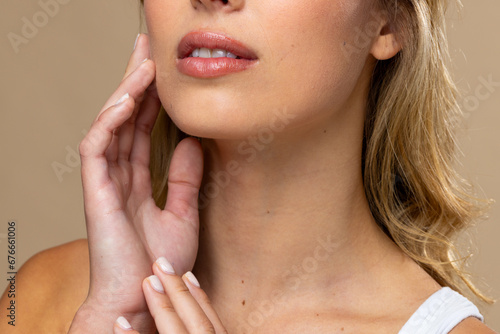 Caucasian woman wearing natural makeup and beige nail polish on beige background