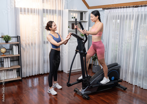 Energetic and strong athletic asian woman running on elliptical running machine at home with workout buddy or trainer. Pursuit of fit physique and commitment to healthy lifestyle. Vigorous