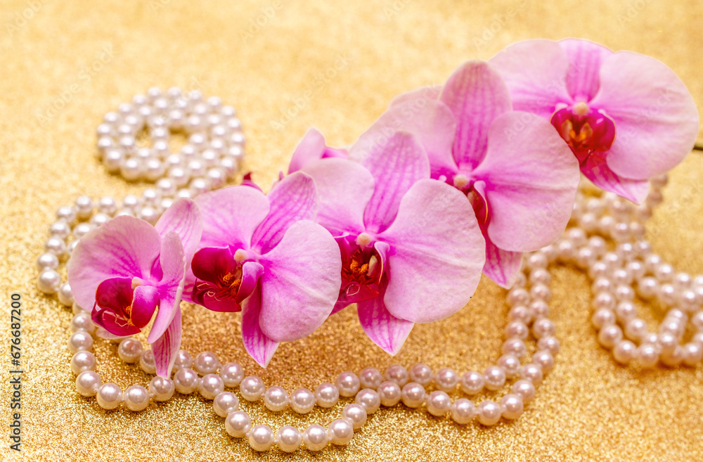 purple Orchid and pearl necklace on a shiny gold background
