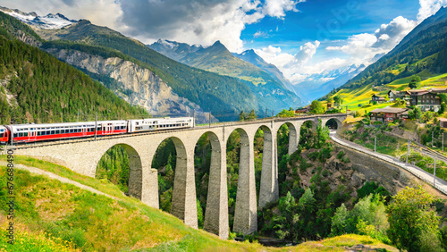 Train moves on railroad bridge in mountain, spring landscape. Switzerland. Red train of Bernina Express on railroad bridge in mountains. photo