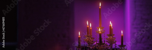 Candelabra with candles in a purple backlit background. Creepy or romantic atmosphere concept. Banner with copy space.
