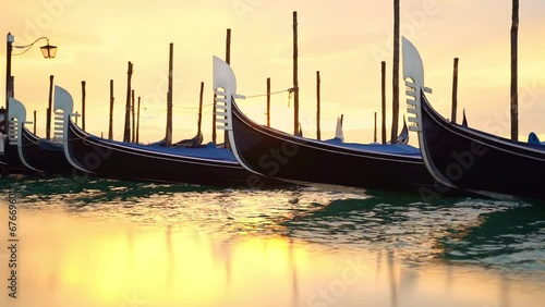 Gondolas in venice in the golden light of dawn with reflection on the stone shore