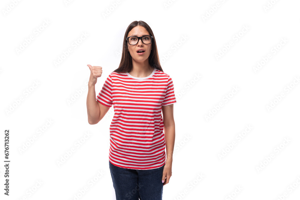 young cute brunette woman with glasses dressed in a striped t-shirt tells the news pointing her finger on a white background with copy space young cute brunette woman with glasses dressed in a striped t-shirt tells the news pointing her finger on a white background with copy space