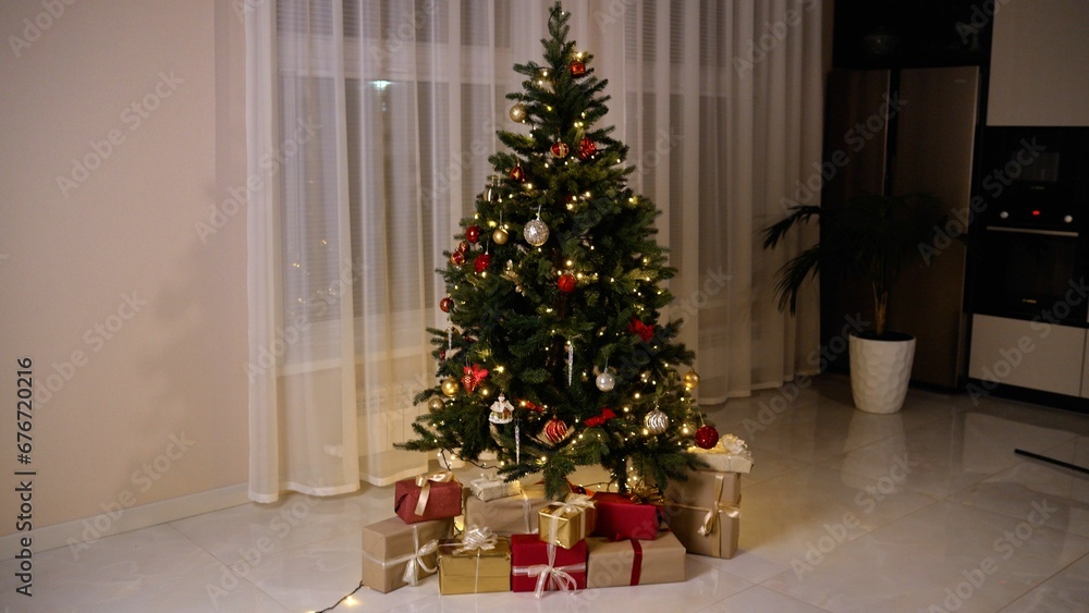 New Year's gifts in designer paper and bright ribbons under the tree on the floor on New Year's Eve. Modern interior of a Christmas room with a decorated Christmas tree and gifts.