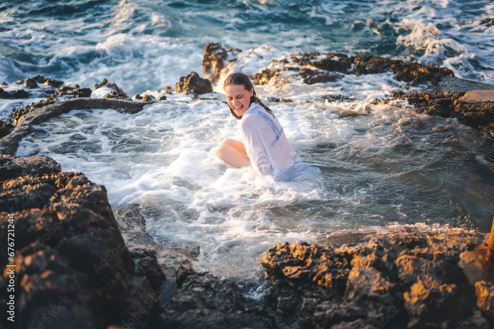 Young cheerful relaxed woman in a white shirt in a natural sea bath on the seashore. Thalassotherapy wellness concept