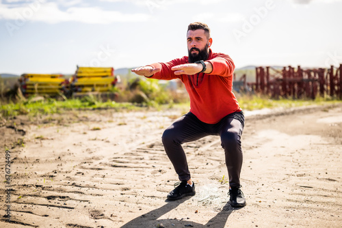 Young man is exercising outdoor. He is doing squats.