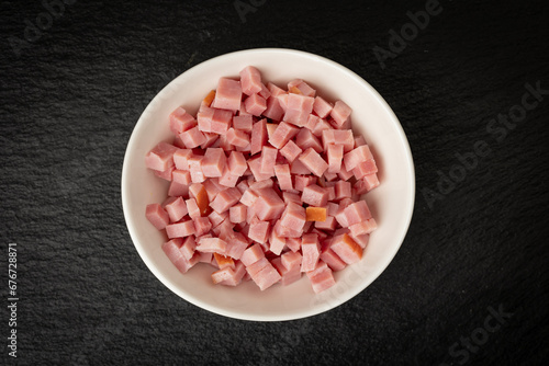 White bowl filled with diced in small cubes ham on black background