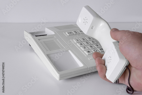 Desk phone 80s, 90s. Push-button dialing. White. Isolated on white table with a hand of man photo