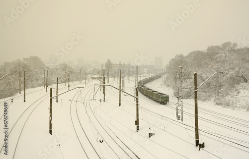 A long train of freight cars is moving along the railroad track. Railway landscape in winter after snowfall