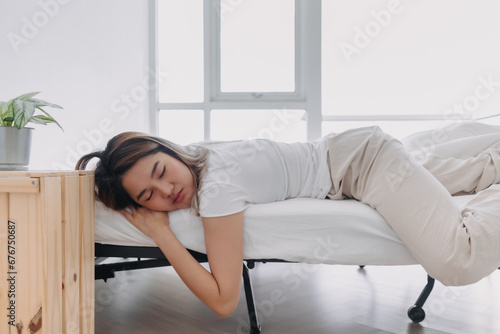 Asian Thai woman sleeping face down on her stomach, lying on white bed, having good dream, drowsy in the morning in apartment room.