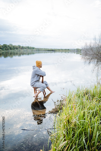 Man sitting on an old wooden chair ankle in the water, man relaxing in nature by the lake.