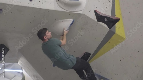Young Caucasian man climbing without a rope in a climbing gym on a high difficulty route with blunt holds. Healthy activity and active living concept