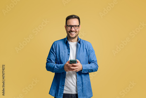 Smiling male professional texting over cellphone while standing confidently on yellow background © Moon Safari