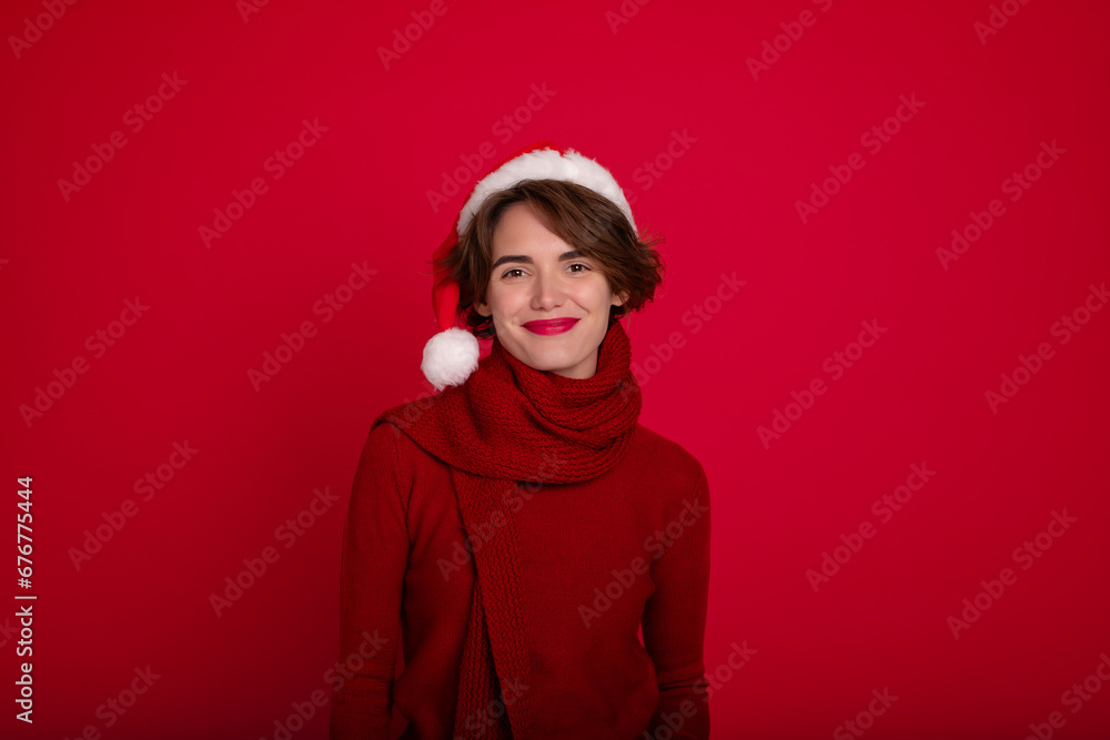Close up portrait of beautiful woman with stylish makeup in Santa hat, red sweater and scarf is posing on bright red background. Merry christmas. Happy new year. Holidays. Party, celebration.