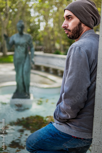 Autumn serenity: Bearded guy, casual attire, leaning on wall, park scenery.