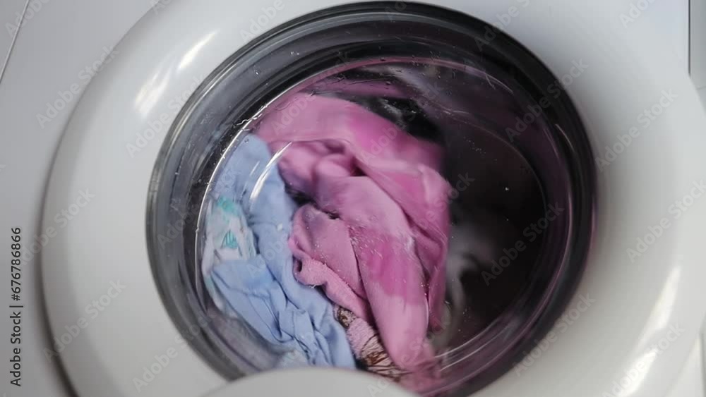 Close up video of washing machine. Laundry machine washing disinfecting, cleaning clothes. White washing machine washes dirty colorful clothes. Washing clothing in domestic washing machine. Close up video of washing machine. Laundry machine washing disinfecting, cleaning clothes. White washing machine washes dirty colorful clothes. Washing clothing in domestic washing machine.