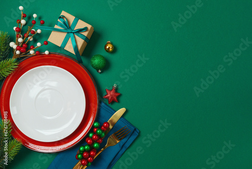 Christmas table decoration with plate, gift box and ornaments on green background. Elegant template for holiday card, invitation and design