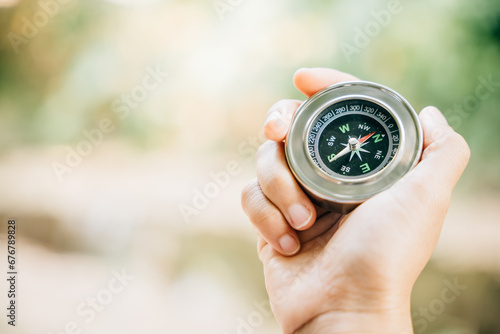 Hiker searches for direction in the forest holding a compass to overcome confusion. The compass in the hand signifies exploration and finding one way in the wilderness.