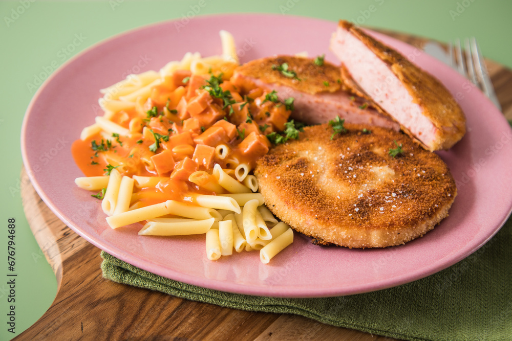 Jägerschnitzel nach DDR GDR Rezept mit Jagdwurst paniert, Makkaroni Penne Nudeln, Tomatensoße, Petersilie mit pink rosa Teller, Besteck, Holzbrett, Serviette und grünen Hintergrund Jägerschnitzel nach DDR GDR Rezept mit Jagdwurst paniert, Makkaroni Penne Nudeln, Tomatensoße, Petersilie mit pink rosa Teller, Besteck, Holzbrett, Serviette und grünen Hintergrund