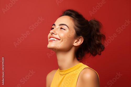 A beautiful young woman with wavy dark hair in a yellow blouse on a red background smiles and looks to the side.