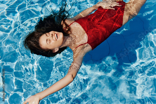 Young woman in the pool in a red swimsuit with a beautiful smile lying on the water and swimming in the sun swimming in the pool, the concept of relaxing on vacation.