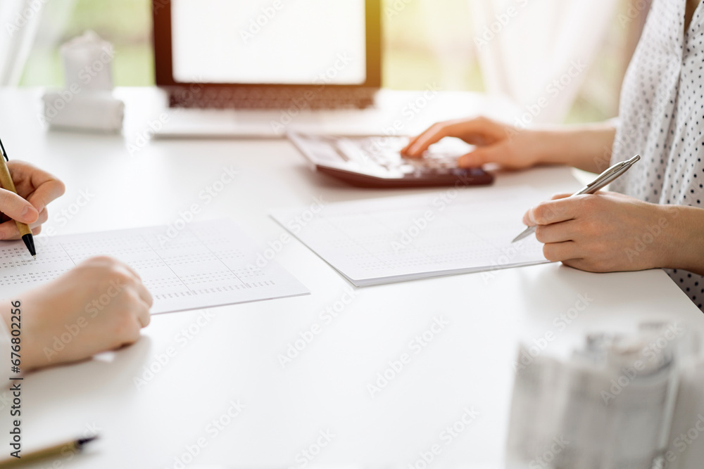 Two accountants using a calculator and laptop computer for counting taxes or revenue balance while rolls of receipts are waiting to be calculating. Business audit and taxes concepts Two accountants using a calculator and laptop computer for counting taxes or revenue balance while rolls of receipts are waiting to be calculating. Business audit and taxes concepts