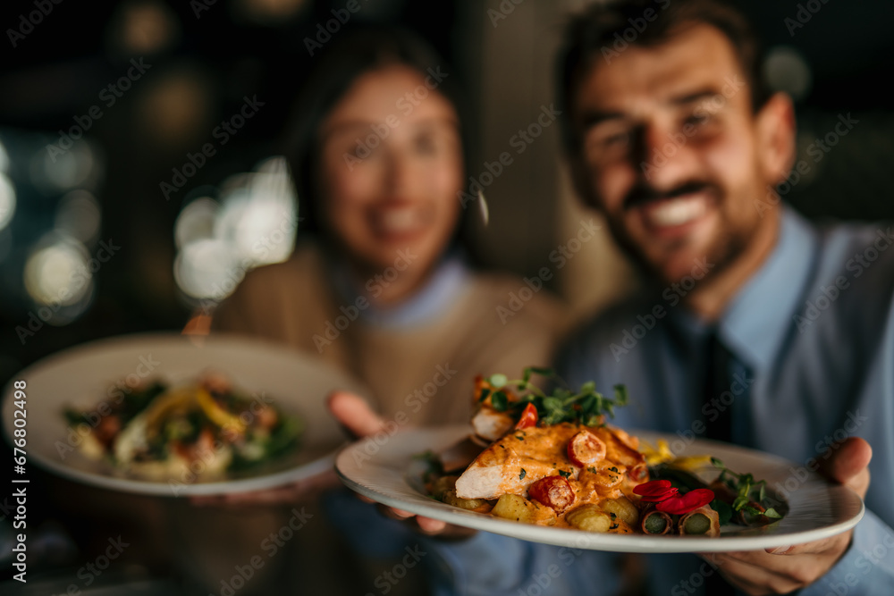 Portrait of two smiling people sitting and holding a plate of food in the restaurant. Portrait of two smiling people sitting and holding a plate of food in the restaurant.