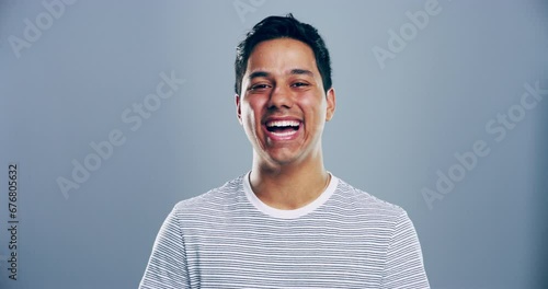 Happy, face and man laughing in a studio for funny, comic and silly joke in conversation. Smile, excited and portrait of young male model from Mexico with goofy expression by gray background. photo