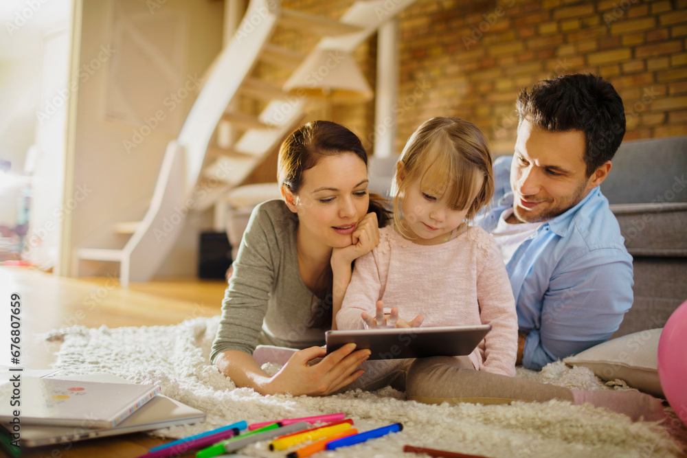 Young family with little daughter watching funny video or cartoons on tablet at home