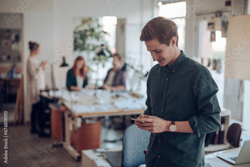 Young man standing using smartphone in startup office