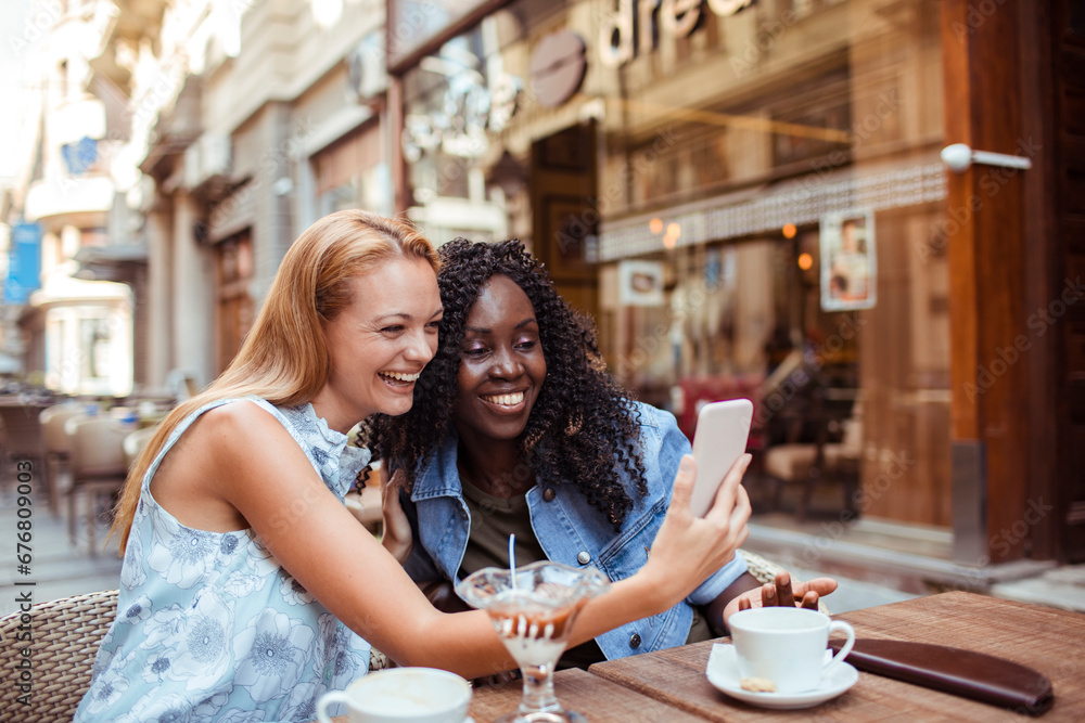 Two young women friends taking selfie in city cafe