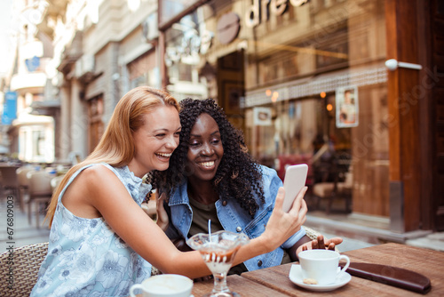 Two young women friends taking selfie in city cafe