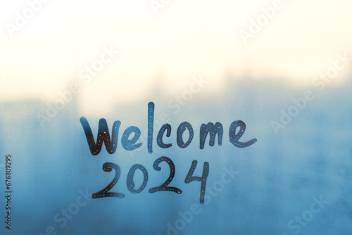 lettering Welcome and numbers 2024 of new year paint with finger on splashed by rain foggy glass on blue and sunset window photo