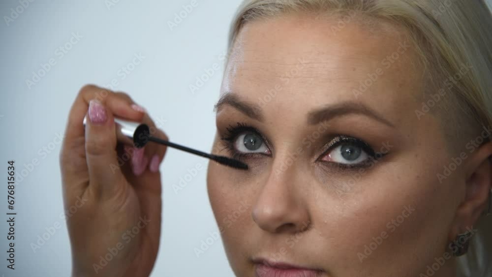 Close-up view of make-up artist applying mascara using wand applicator on eyelashes of adult blond woman in beauty salon. Soft focus. Real time handheld video. Make-up and beauty theme. Close-up view of make-up artist applying mascara using wand applicator on eyelashes of adult blond woman in beauty salon. Soft focus. Real time handheld video. Make-up and beauty theme.