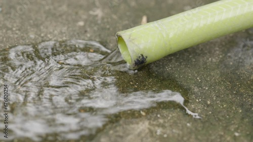 A green water hose is running along the concrete floor. waste of water to use it unnecessarily. photo