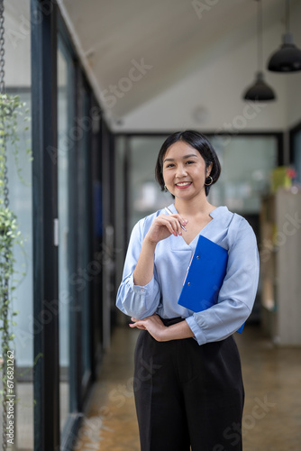 Vertical image of standing businesswoman holding a pen and document clipboard under her arm.