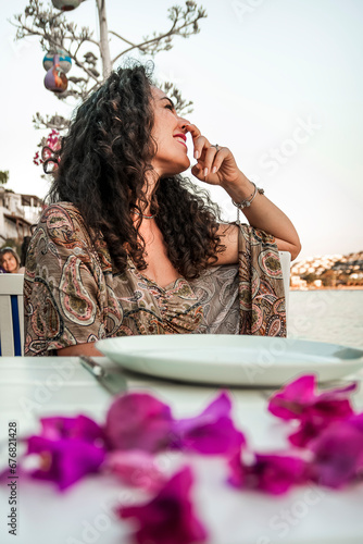 beautiful curly haired mediterranean woman smiles sitting at a restaurant table
