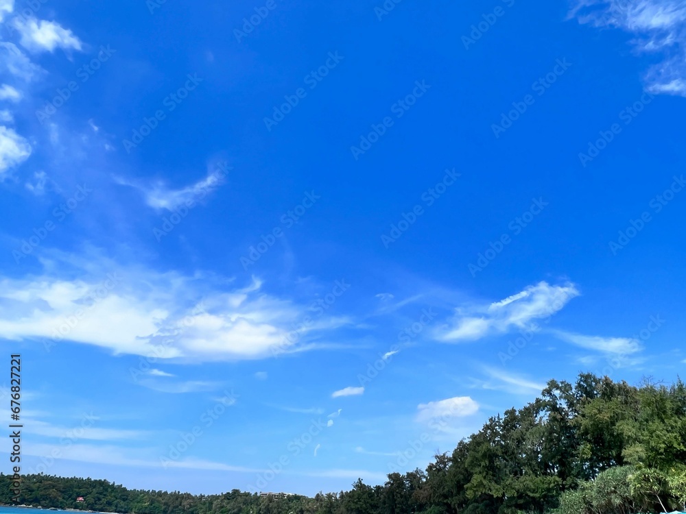 Image of a blue sky from the beach and mountain covered by trees.
