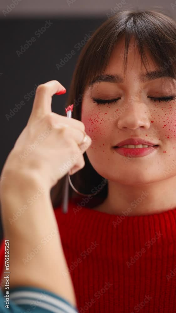 Asian model girl closed her eyes and smiles as the make-up artist splashes red drop paint on her face. art makeup vertical video. blush Asian model girl closed her eyes and smiles as the make-up artist splashes red drop paint on her face. art makeup vertical video. blush