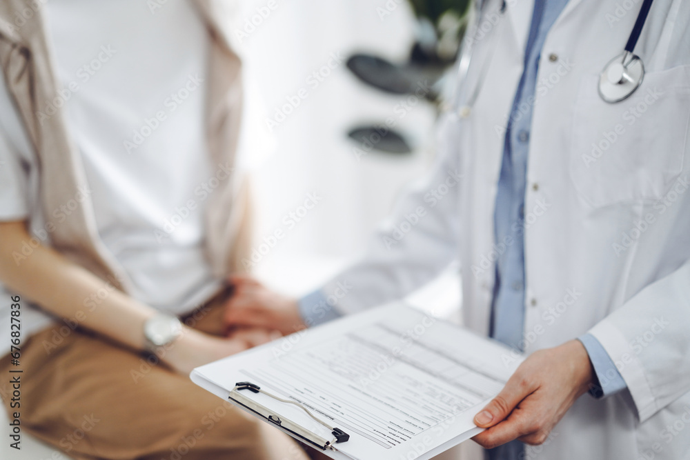 Doctor and patient discussing health exam results. Friendly physician reassuring a young woman by one hand while keeping clipboard with medical papers in another. Medicine concept Doctor and patient discussing health exam results. Friendly physician reassuring a young woman by one hand while keeping clipboard with medical papers in another. Medicine concept