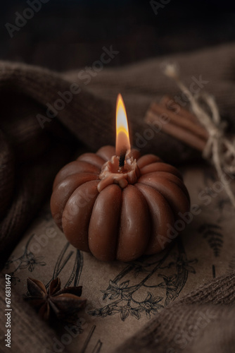 A candle in the shape of a pumpkin on a wooden background