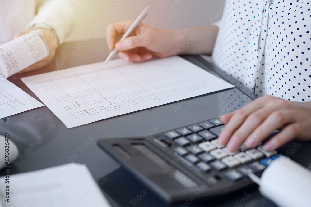 Two accountants use a calculator and laptop computer for counting taxes or revenue balance. Business, audit, and taxes concepts Two accountants use a calculator and laptop computer for counting taxes or revenue balance. Business, audit, and taxes concepts