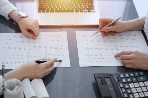 Two accountants use a calculator and laptop computer for counting taxes or revenue balance. Business, audit, and taxes concepts photo