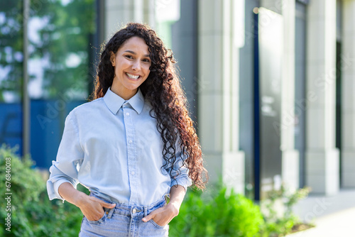 Portrait of a happy Indian woman working in the office standing outside with her hands in her pockets looking at the camera and smiling, a student in a good mood in the morning before studying. photo