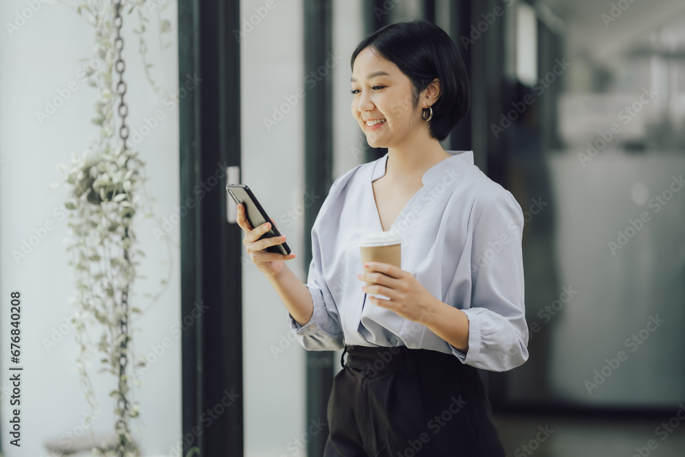 Beautiful young asian businesswoman using smartphone and holding coffee. Woman using mobile phone, watching movie, listening to music, shopping Beautiful young asian businesswoman using smartphone and holding coffee. Woman using mobile phone, watching movie, listening to music, shopping