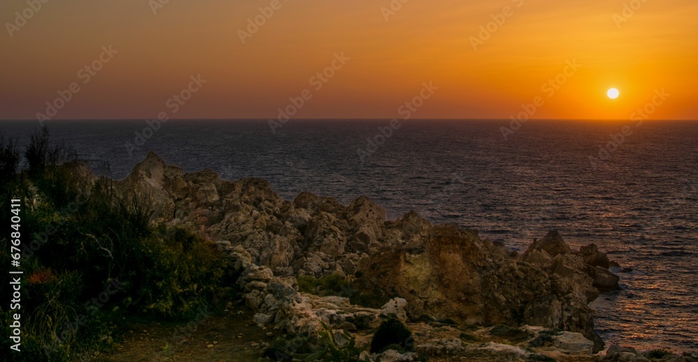 Landscapw scene of rocky coast by the sea with orange sunset sky on the horizon Landscapw scene of rocky coast by the sea with orange sunset sky on the horizon