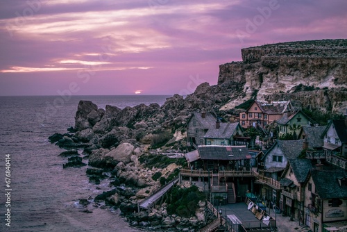 Landscape scene of Popeye Village houses by the sea with purple sunset sky in Mellieha, Malta photo