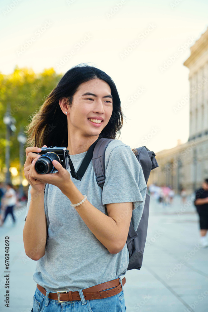 Asian male tourist smiling with his camera while sightseeing in Madrid, Spain.