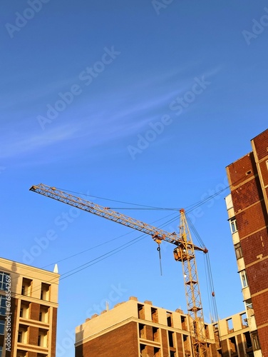 Crane surrounded by tall brown buildings in a city under a bright blue sky