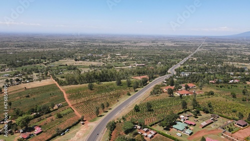 Drone shot of a road in a green landscape with small houses and trees under blue sky